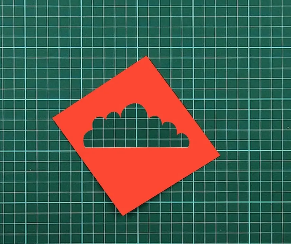 A red paper cut out of a cloud on top of green paper.