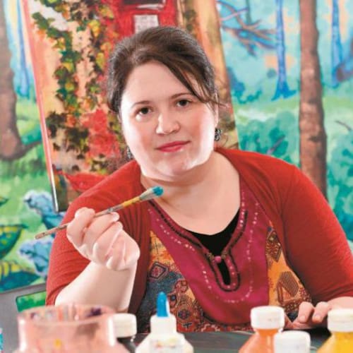 A woman sitting at a table with paint brushes.