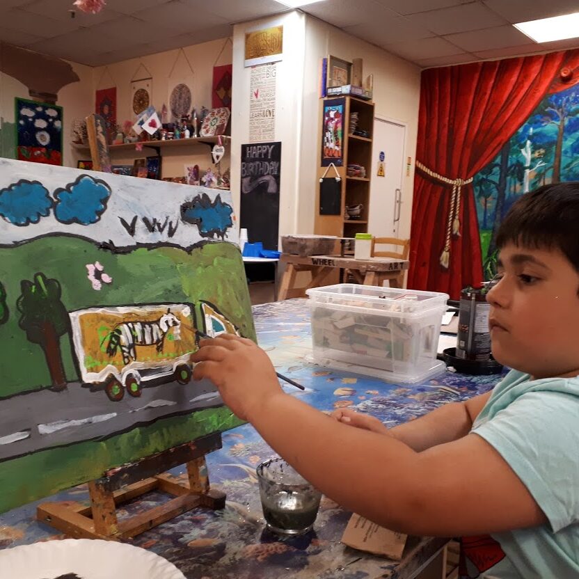 A boy is painting on an easel in his room.